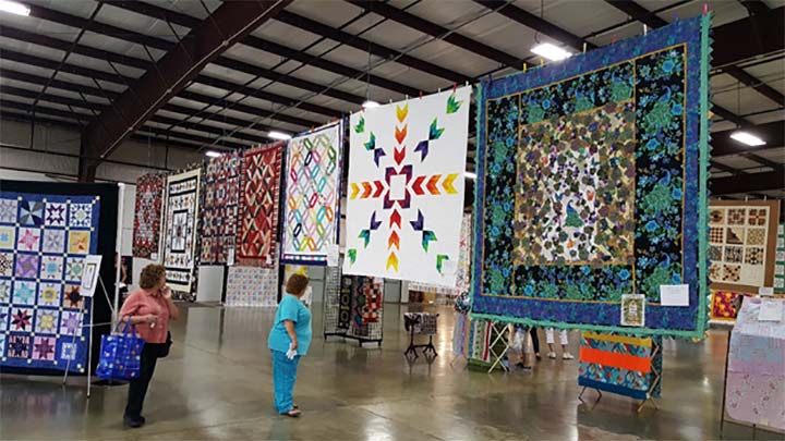 Supplied Photo: Quilts hanging in the Tom Raper Center with two women looking at them.