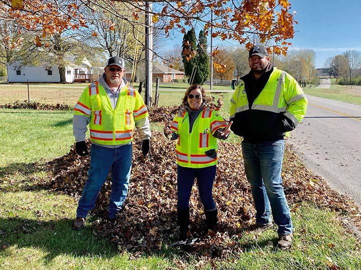 Supplied Photo:  2 men and 1 woman in reflective vests in front of a pile of fall leaves.