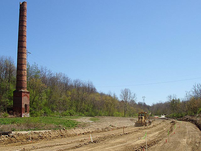 Photo of grader working on road in front of the remains of the smokestack from the Starr-Gennett Company.