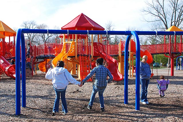 Teenage couple holds hands while swinging at the park.